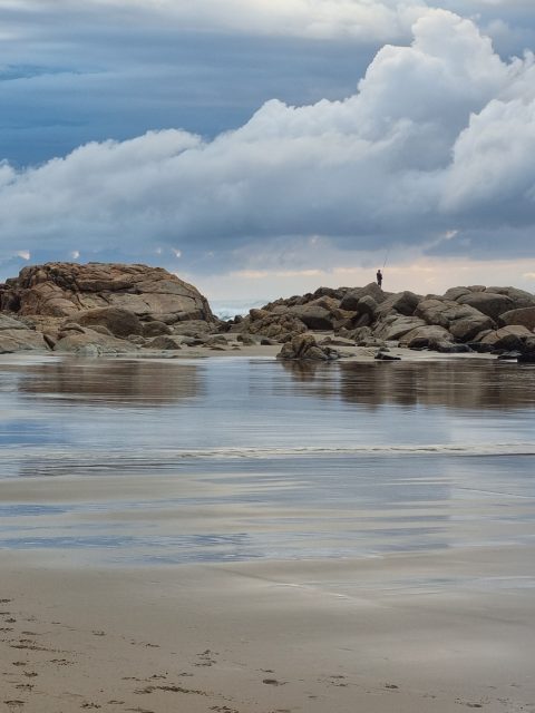 Lone angler silhouetted on coastal rocks at dusk