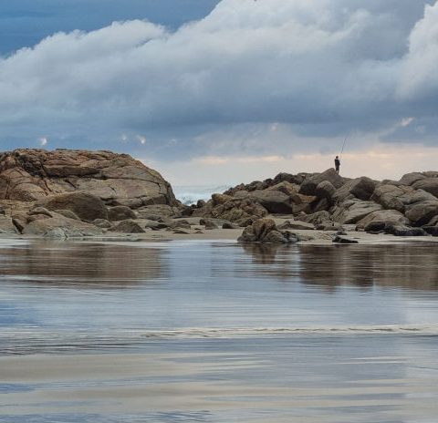 Lone angler silhouetted on coastal rocks
