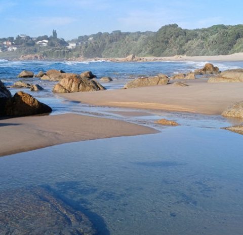 Clear tide pool between boulders with the village and forest beyond